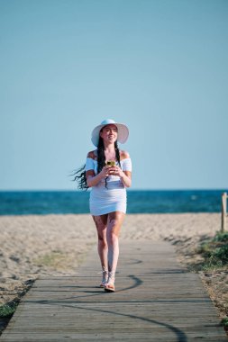 Woman with vitiligo smiling while using mobile phone walking on walkway at the beach. Summer and technology concept.