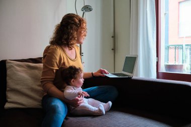 Woman working with laptop from home while taking care of her baby. Technology, business and maternity concept.