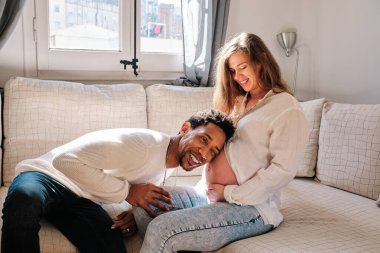 Man listening baby sound on his pregnant wife belly at home. Relationship and pregnancy concept.