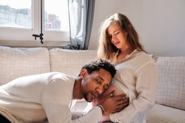 Man leaning his head on his pregnant wife belly to listen the baby. Relationship and pregnancy concept.