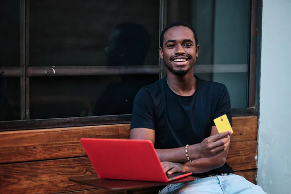 Hombre Mirando Cámara Sonriendo Mientras Utiliza Tarjeta Crédito Ordenador Portátil —  Fotos de Stock