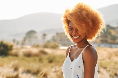 Dışarıdaki kameraya gülümseyen afro saçlı bir kadının portresi.