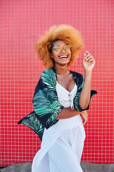 Happy african woman laughing while posing with summer clothes with a pink wall as a background