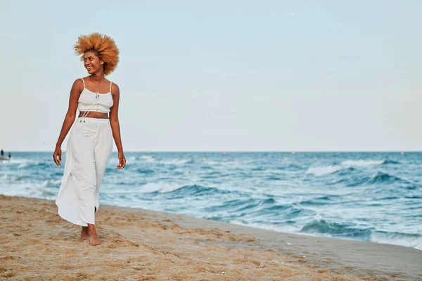 Afro Kobieta Białych Ubraniach Spaceruje Wzdłuż Plaży Podczas Zachodu Słońca — Zdjęcie stockowe