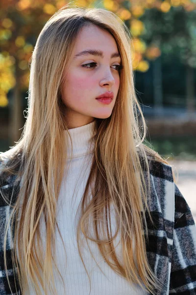 Parkta dikkati dağılmış sarışın bir kadının dikey yakın portresi.