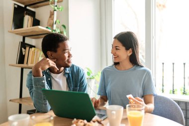 İki çok kültürlü arkadaş evden online alışveriş yapmak için kredi kartı kullanıyor.