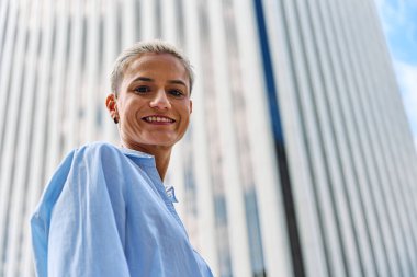 Gülümseyen bir iş kadınının alçak açılı portresi gökdelenin yanındaki kameraya bakıyor.