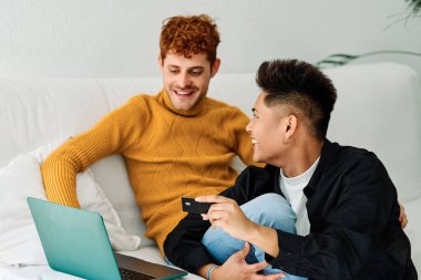 Kanepede dizüstü bilgisayar kullanarak internetten alışveriş yapan eşcinsel bir çiftin portresi.