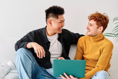 Koltukta dizüstü bilgisayar kullanan mutlu, etnik çeşitlilikte eşcinsel bir çiftin portresi.