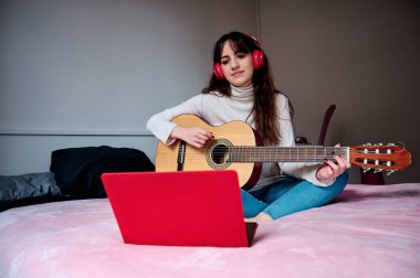 Kadın dizüstü bilgisayarıyla online ders alırken gitar çalmayı öğreniyor. Müzik ve teknoloji konsepti.