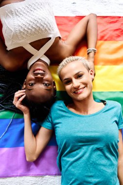 LGBT bayraklarında yatıp kameraya bakan lezbiyen bir çiftin üst görünüm portresi