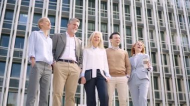 Düşük açılı yavaş çekim videosu ve bir grup mutlu iş adamının finans binasının önünde yan yana durması.