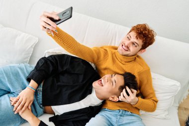 Çok ırklı eşcinsel bir çiftin evdeki kanepede selfie çekerken en iyi görüntüsü.