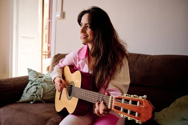 自宅でソファに座ってギターを練習しながら微笑むリラックスした女性 音楽の概念 — ストック写真
