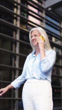 Yaşlı iş kadını telefonda gökdelen ayarlı dikey çerçevede konuşuyor - finansal konsept