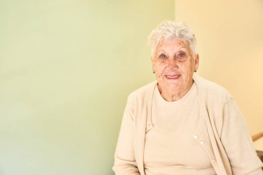 Bir klinikte kameraya gülümseyen yaşlı ve mutlu bir kadının fotokopisi.
