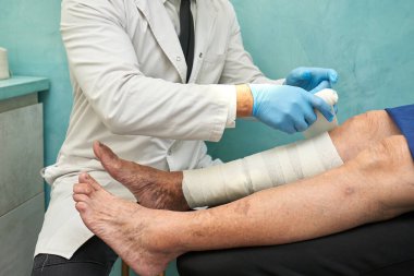 Doktor yaşlı bir kadının bacaklarına sargı bezi sararak dolaşım yapıyor.