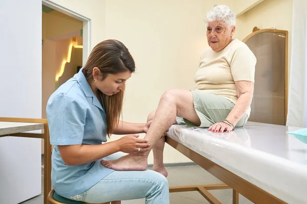 Doctor examining the legs of an old women in a clinic