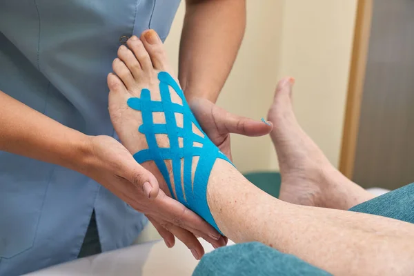 Close-up of a female doctor applying blue kinesio tape on womans foot