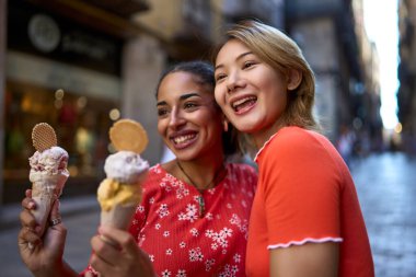 Sokakta birlikte dondurma yiyen çok kültürlü lezbiyen bir çiftin yan görüntüsü.