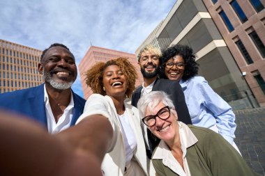 Bir grup mutlu çoklu etnik meslektaşın açık havada selfie çekerken ön açı düşük.