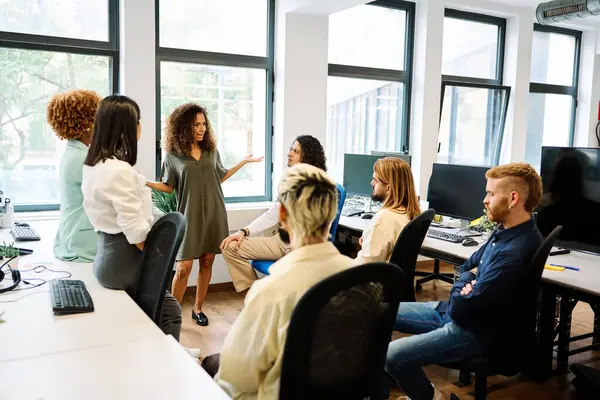 Female leader standing speaking to colleagues sitting on a coworking