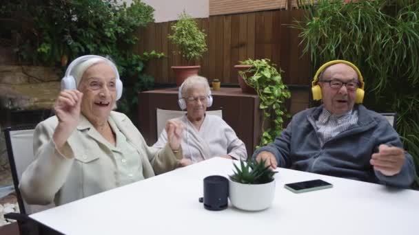 三个快乐的老年人在疗养院用耳机和手机听音乐的视频 — 图库视频影像
