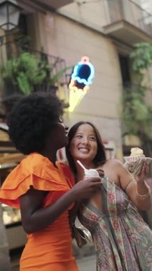 İki genç çoklu etnik turistin şehirde dondurma yerken çekilmiş dikey videosu.
