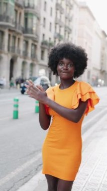 Afrikalı genç bir kadının sokakta dans edip alkışladığı dikey bir video.