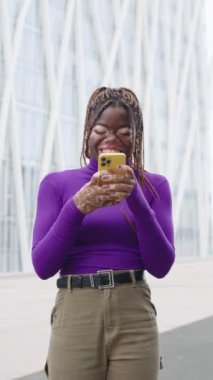 Vitiligo 'su olan Afrikalı bir kadının dikey yavaş çekim videosu şehirde telefon duruşu yaparak gülmeye başladı.
