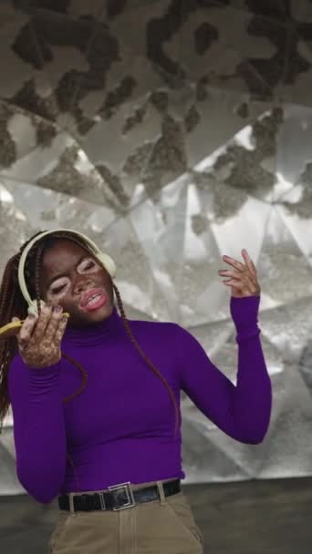 在城市里 一个有着白垩风的非洲女人用耳机唱歌和听音乐的垂直慢动作视频 — 图库视频影像