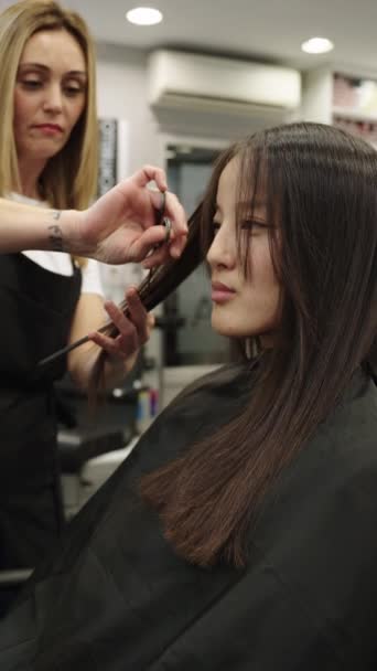 一位美发师在沙龙里剪掉一位头戴斗篷的中国妇女的长发的垂直慢镜头 — 图库视频影像