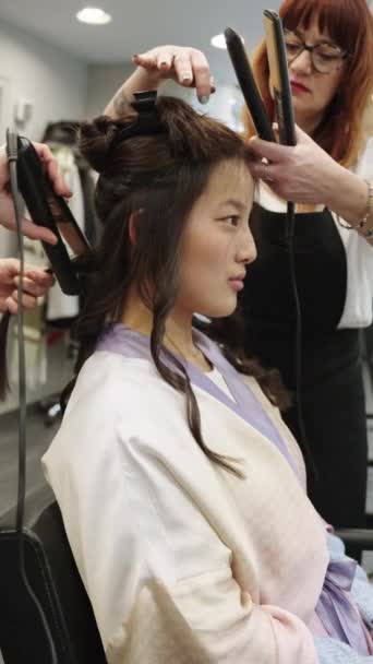 两个发型师在沙龙里卷曲一位亚洲美女的头发的垂直慢镜头 — 图库视频影像