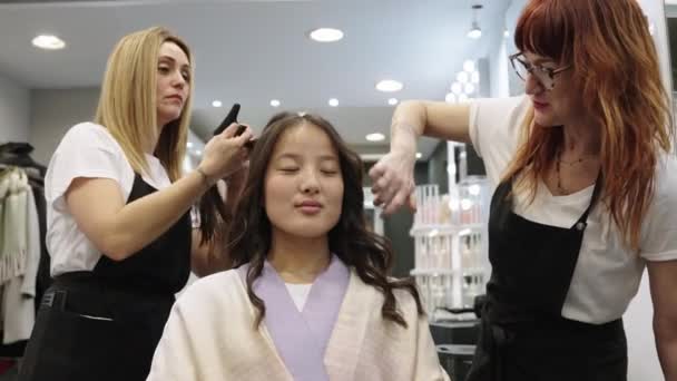 中国の女の子の髪を平らな鉄で治す2人の白人美容師のスローモーションビデオ — ストック動画