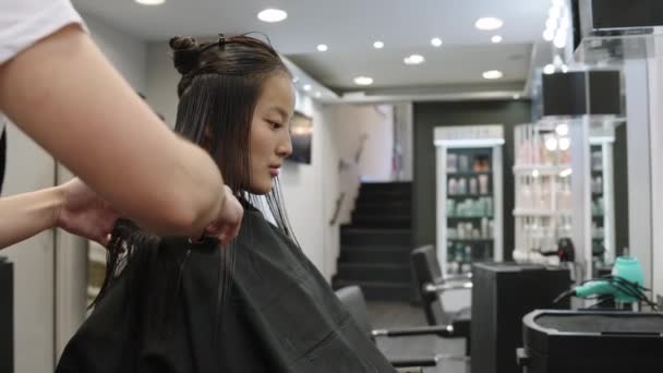 サロンで中国の若い女性の髪をトリミングするヘアスタイリストのスローモーションビデオ — ストック動画