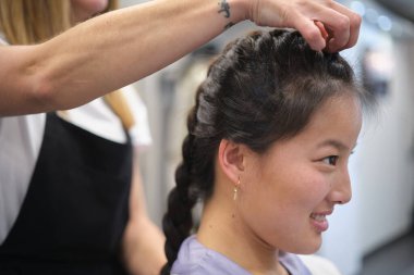 Kuaförde Çinli bir kadının örgüsünü düzenleyen dikkatli bir kuaföre yakın plan.