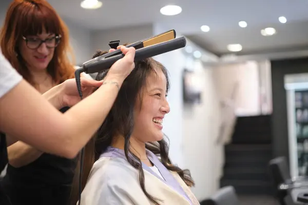 Chinese woman laughing while hairdressers curling her hair in a salon