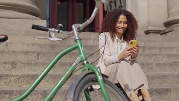 Latin Kadını Merdivenlerde Oturuyor Yanında Bisikletiyle Telefonuna Bakıyor — Stok video