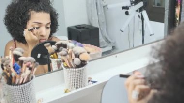 Transeksüel bir kadının göz makyajını yavaş çekimde yapması. Evdeki banyoda oturması.