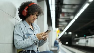 Metro durağındaki bir platformda oturan transseksüel bir insanın cep telefonu kullanması yavaş bir hareket..