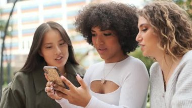 Çok ırklı arkadaşların ve transseksüel kadınların caddede birlikte cep telefonunu kullanmalarının yavaş çekim videosu.