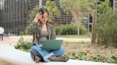 Şehir parkında dizüstü bilgisayar kullanan Asyalı bir kadının yavaş çekim videosu.