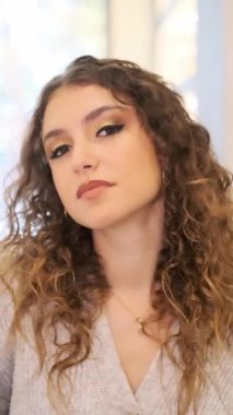 Makyajı bitmiş güzel bir kadının kameraya bakarken dikey yavaş çekim videosu.