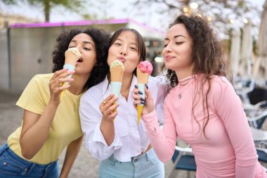 Genç çoklu etnik kadınlar dondurma külahlarını birlikte yiyorlar.