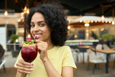 Genç Latin kadın açık terasta pipetle içki içiyor.