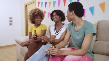 LGBTQIA arkadaşları bir ev partisinde biralarla kanepede sohbet edip gülüyorlar.