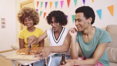 LGBTQIA arkadaşları bir ev partisinde pizza kesiyorlar.