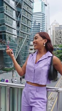 Gülümseyen travesti kadın, Bangkok 'un canlı kentsel manzarasında, kendini ifade etme ve kendine güveni somutlaştıran bir selfie çekiyor.