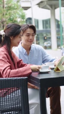 Genç çift açık bir kafede oturuyor, kahvenin tadını çıkarıyor ve birlikte tablet kullanıyorlar.