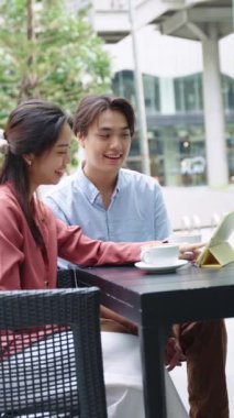 Genç Asyalı bir çift, bir kafede, bir tablet kullanarak ve sohbet ederek rahatlatıcı bir öğleden sonra geçiriyor.